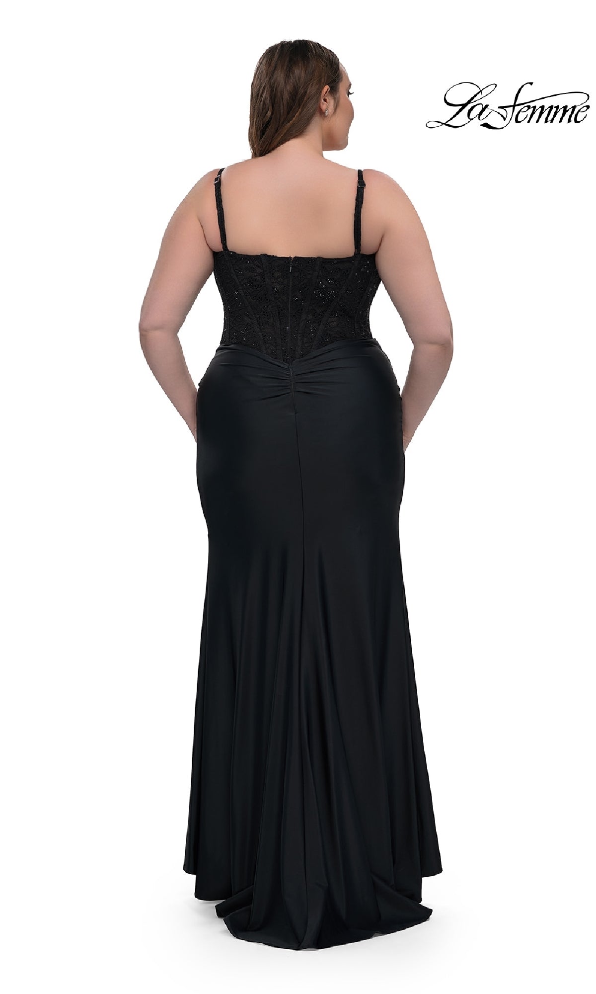 A woman models the Plus-Size Long Corset Prom Dress La Femme 32449, standing with her back to highlight the fitted bodice and flowing skirt of this elegant black formal gown.